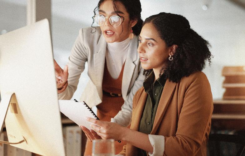 Two business individuals speaking while pointing to a computer screen.