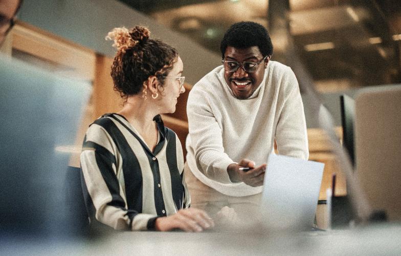 Two colleaguges speaking in an office setting. 