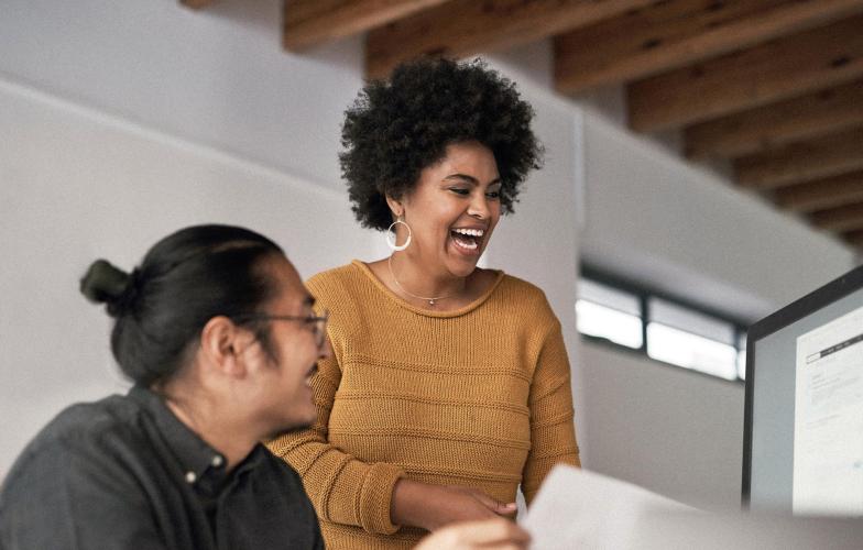 Two individuals laughing while looking at a computer screen.