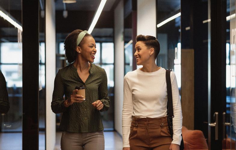 Two individuals laughing while walking together in an office hallway.