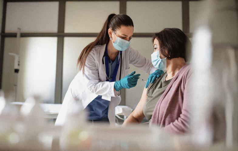 A doctor wearing a mask giving a shot to an elderly patient.