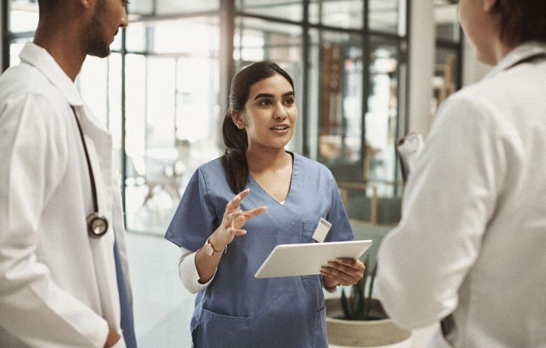 A nurse with an iPad speaking to a small group of young physicians