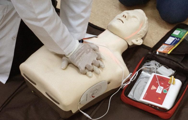 A medical professional applying chest compressions on a CPR dummy with an AED monitor