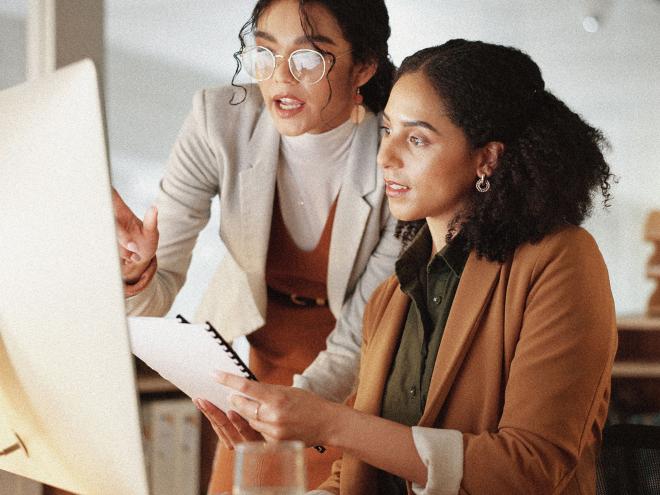 Two business individuals speaking while pointing to a computer screen.