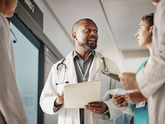 A doctor speaking with three other medical staff in a hospital hallway.