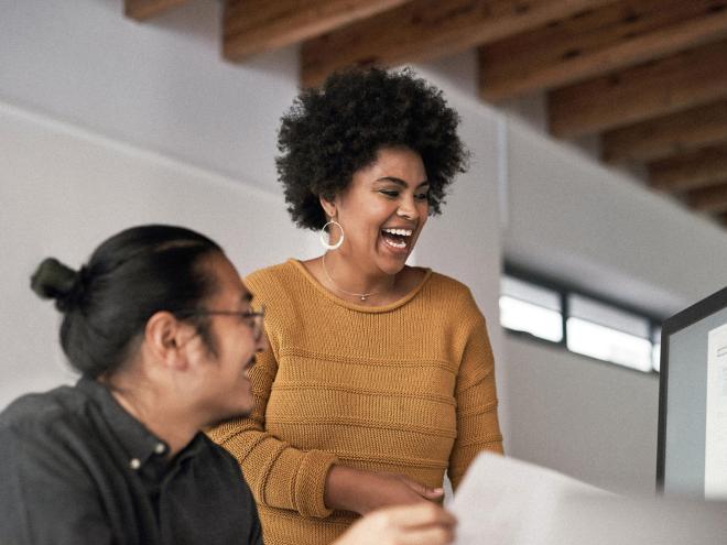 Two individuals laughing while looking at a computer screen.