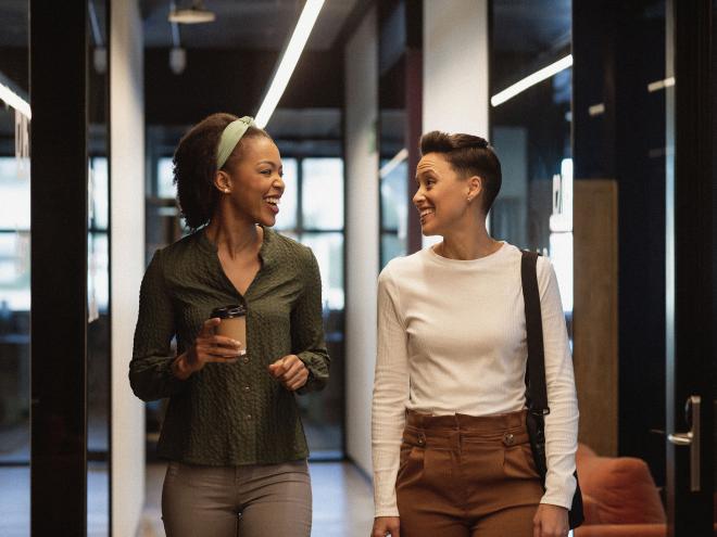 Two individuals laughing while walking together in an office hallway.