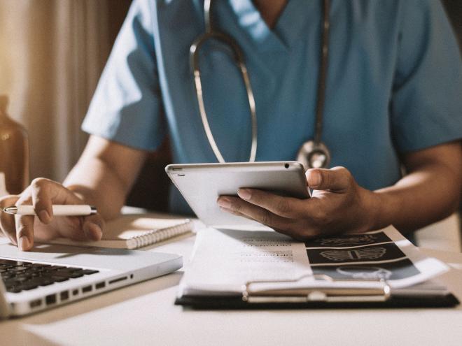 A close up of a doctors hands holding an ipad and doing paperwork.