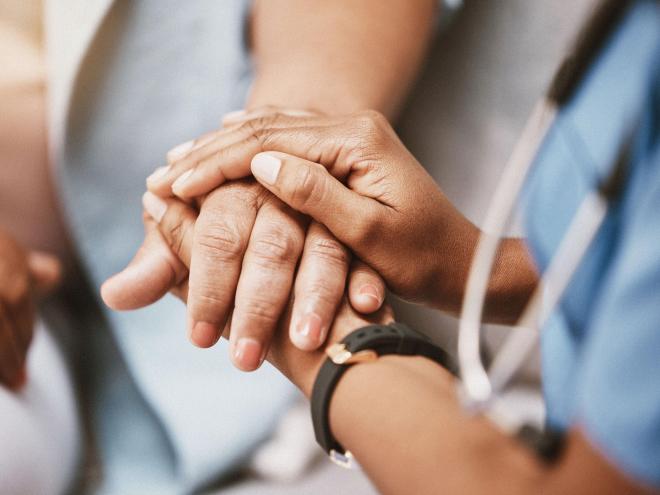 A doctors hands holding a patient's hand between them. 