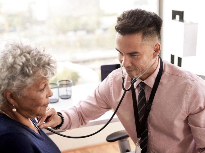 Doctor listening to an elderly patients chest with a stethoscope.
