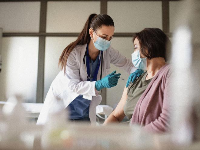 A doctor wearing a mask giving a shot to an elderly patient.