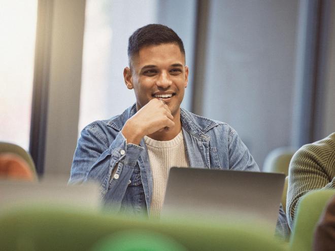 An inidividual sitting in a group setting with a laptop. 