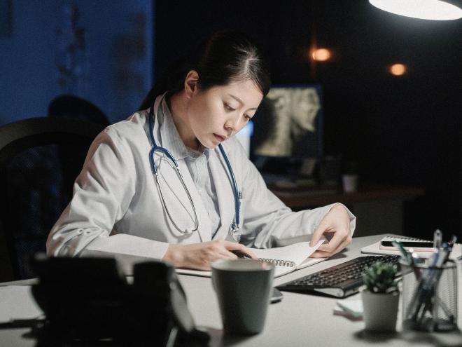 A doctor sitting behind a desk and writing in a notebook. 