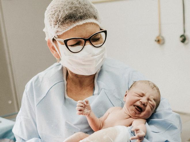 Doctor holding a newborn baby in delivery room.