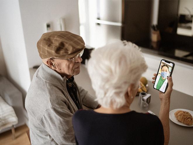 A doctor performing a virtual group medical visit with an elderly couple on a mobile device