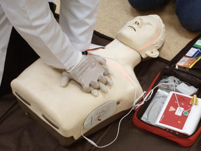 A medical professional applying chest compressions on a CPR dummy with an AED monitor