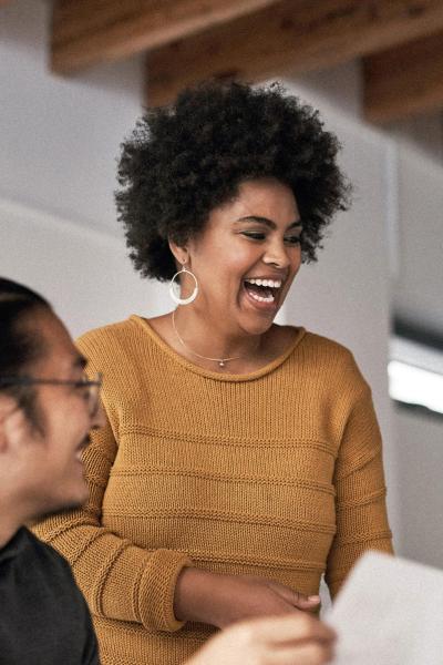 Two individuals laughing while looking at a computer screen.