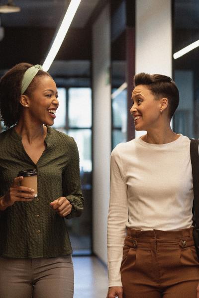 Two individuals laughing while walking together in an office hallway.