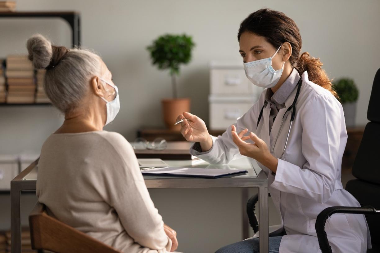Doctors wearing mask speaking to elderly patient.