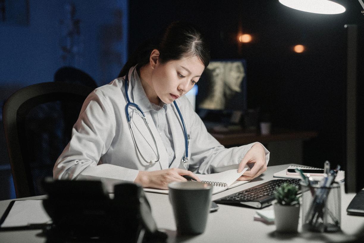 A doctor sitting behind a desk and writing in a notebook. 