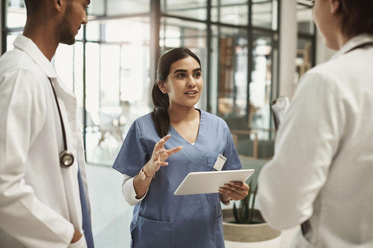 A nurse with an iPad speaking to a small group of young physicians