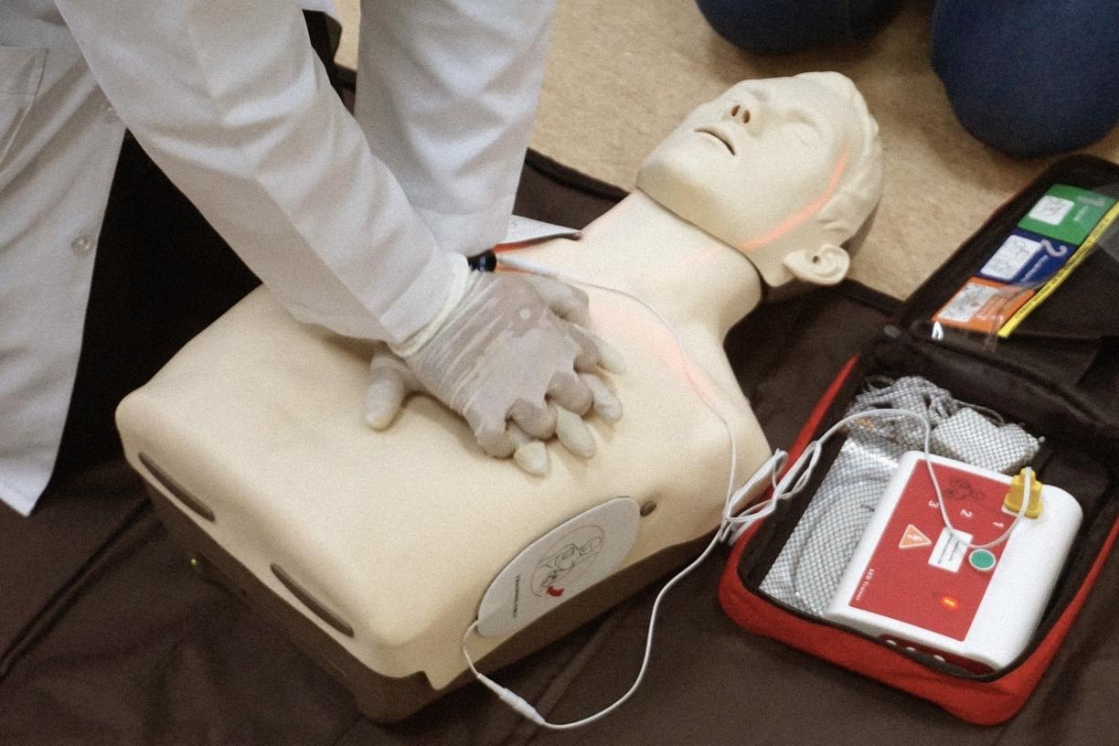 A medical professional applying chest compressions on a CPR dummy with an AED monitor